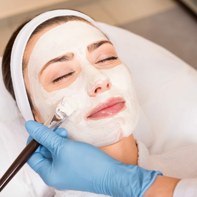 beautician applying cosmetic mask on woman face with cosmetic brush at beauty salon beautician applying cosmetic mask on woman face with cosmetic brush at beauty salon